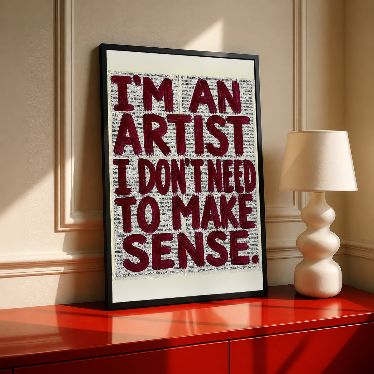 Framed newsprint quote poster with burgundy text: I’M AN ARTIST, I DON'T NEED TO MAKE SENSE