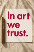 Typography wall print with red 'In art we trust.' text on off-white background.