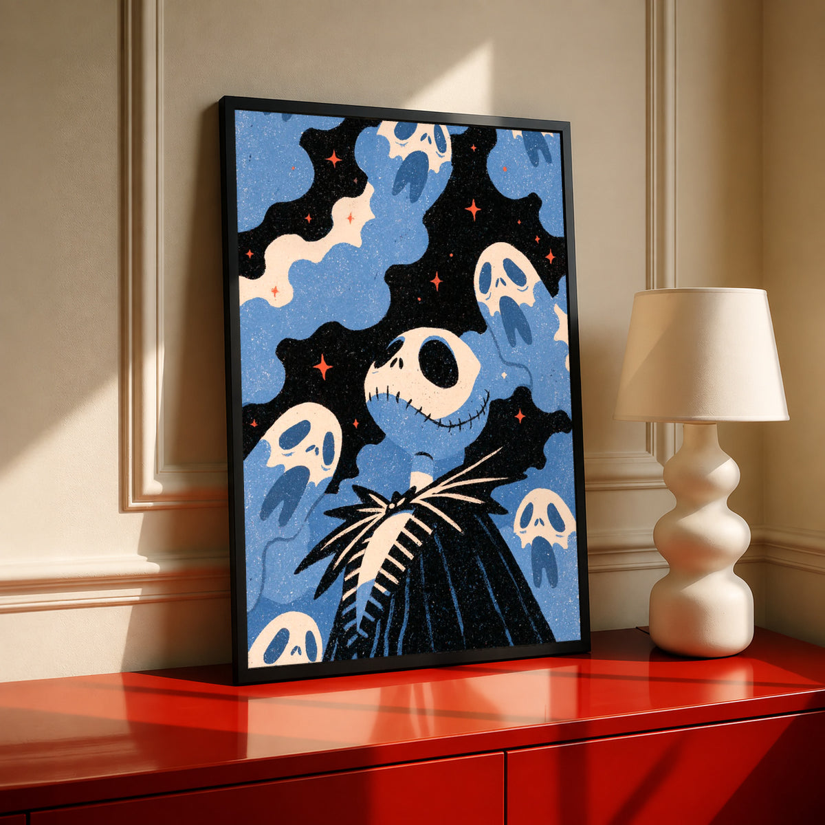 Jack Skellington surrounded by blue ghosts, cream clouds and tiny orange stars on black in a black frame on a red console beside a sculptural cream lamp