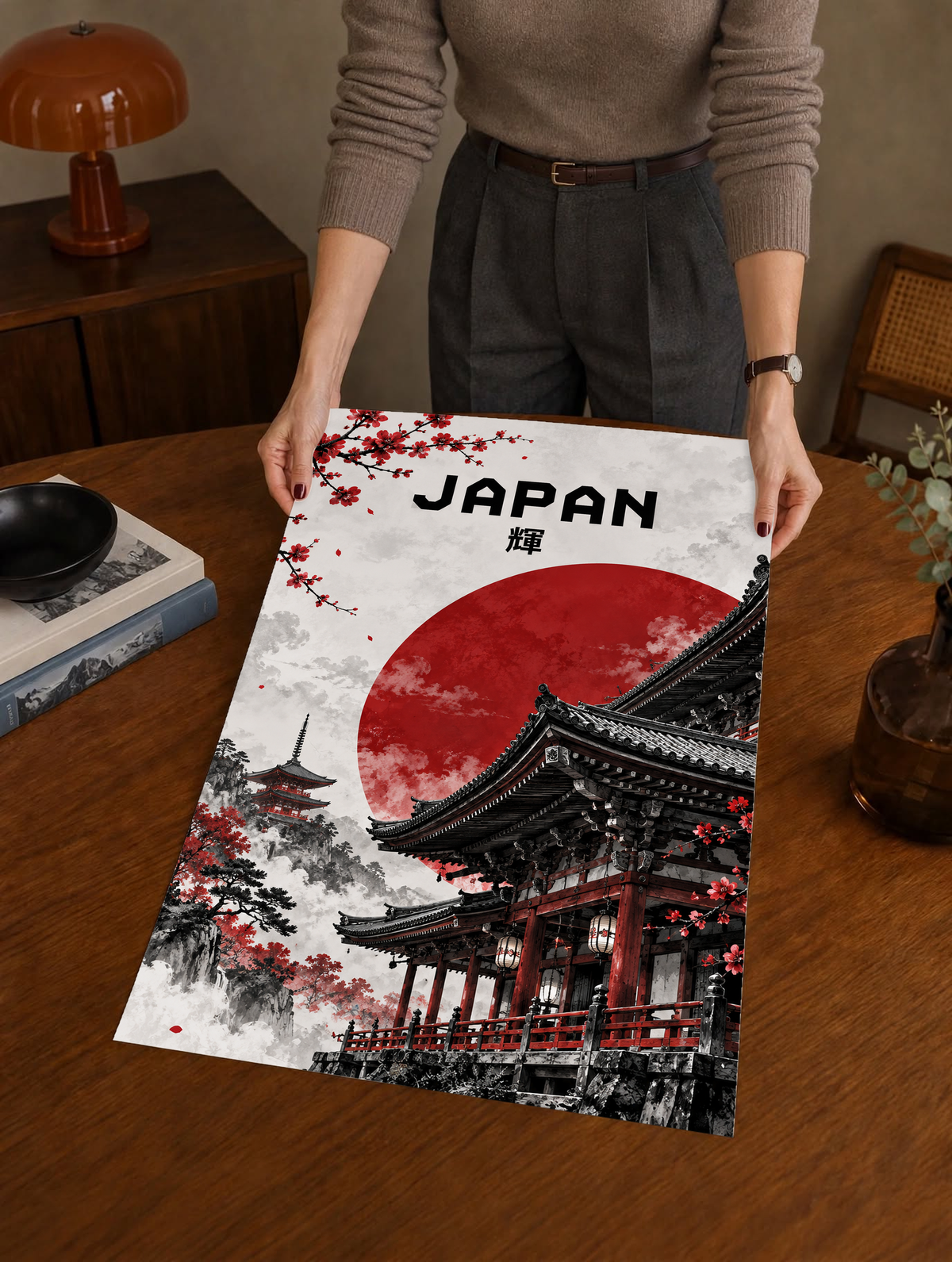 Person holding large temple poster with red sun, black architecture, and cherry blossom branches.