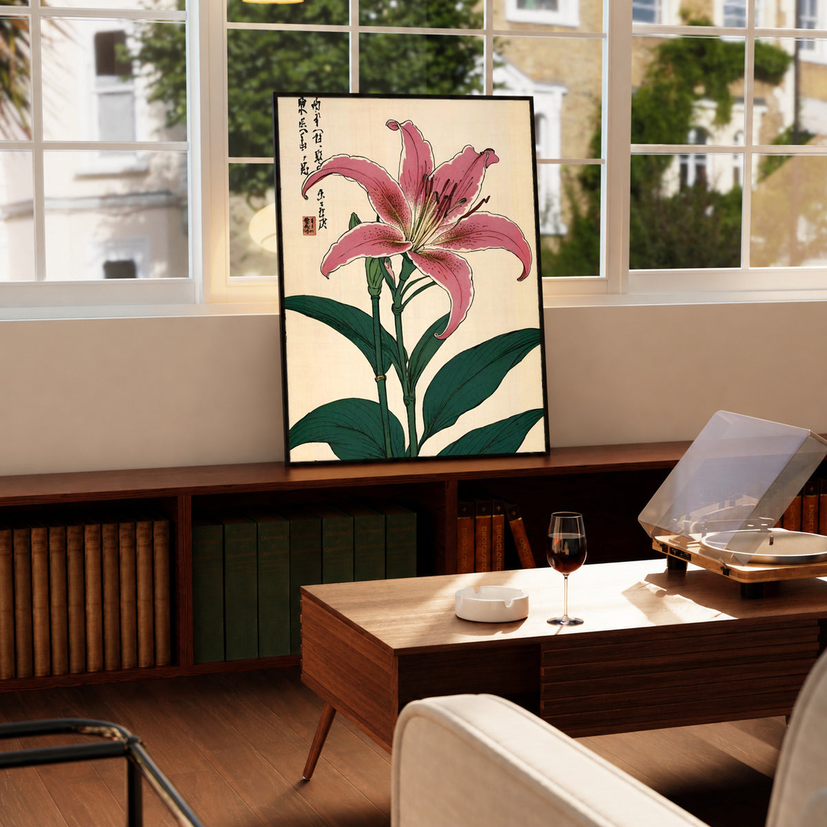 Pink lily with dark green leaves Japanese calligraphy and a red seal on cream in a black frame on a wooden cabinet beside a window and record player