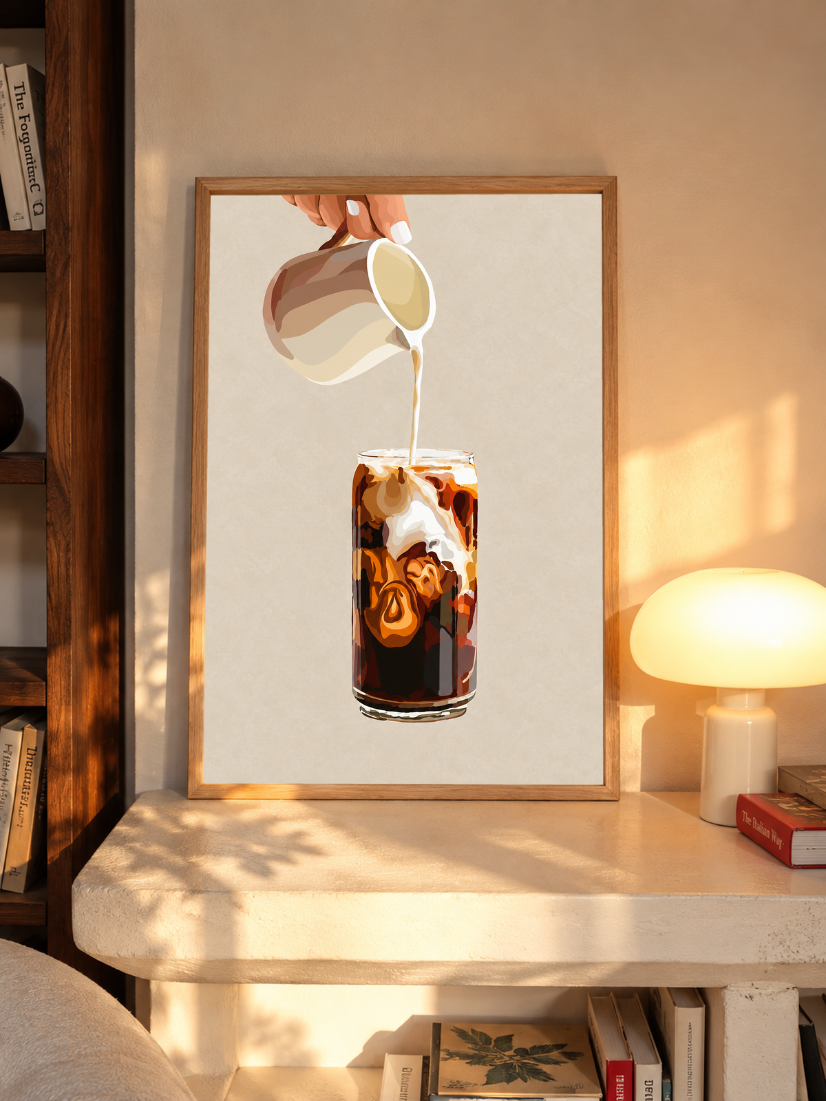 Mockup im Eichenrahmen auf einem Regal neben einer leuchtenden Tischlampe: Eiskaffeeillustration mit einer Hand, die Milch aus einem gestreiften Kännchen in ein hohes Glas gießt, und cremefarbenen Karamellwirbeln auf Beige.