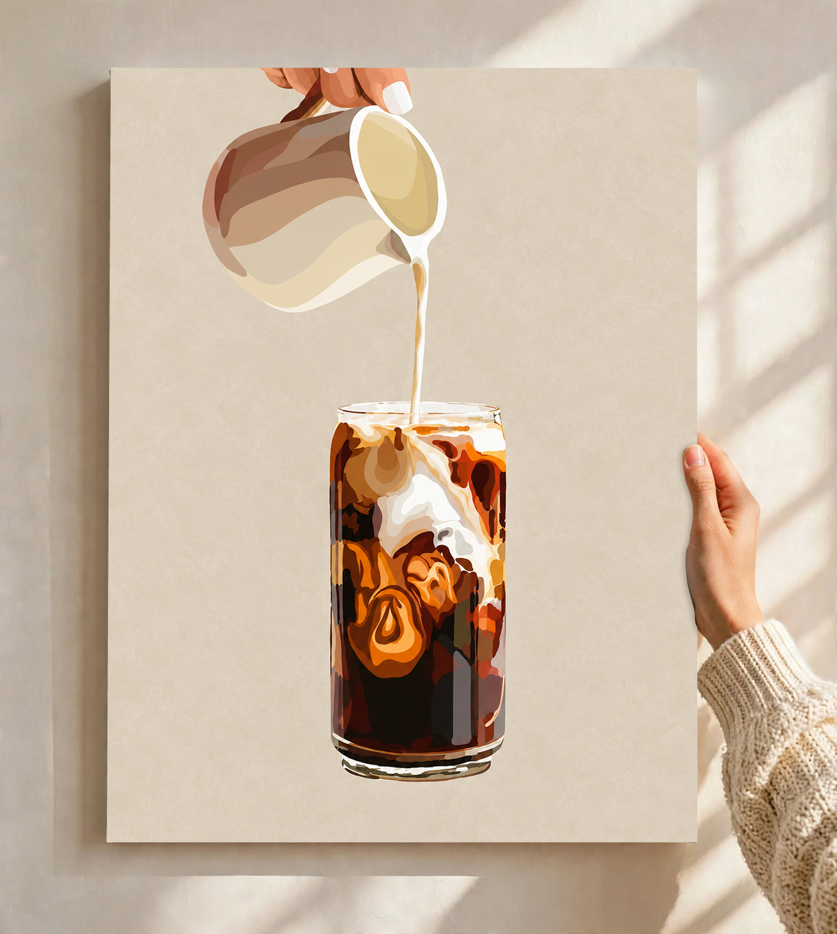 Mockup eines ungerahmten Posters, vor einer hellen Wand im Fensterlicht gehalten: Eiskaffeeillustration mit einer Hand, die Milch aus einem gestreiften Kännchen in ein hohes Glas gießt, und cremefarbenen Karamellwirbeln auf Beige.