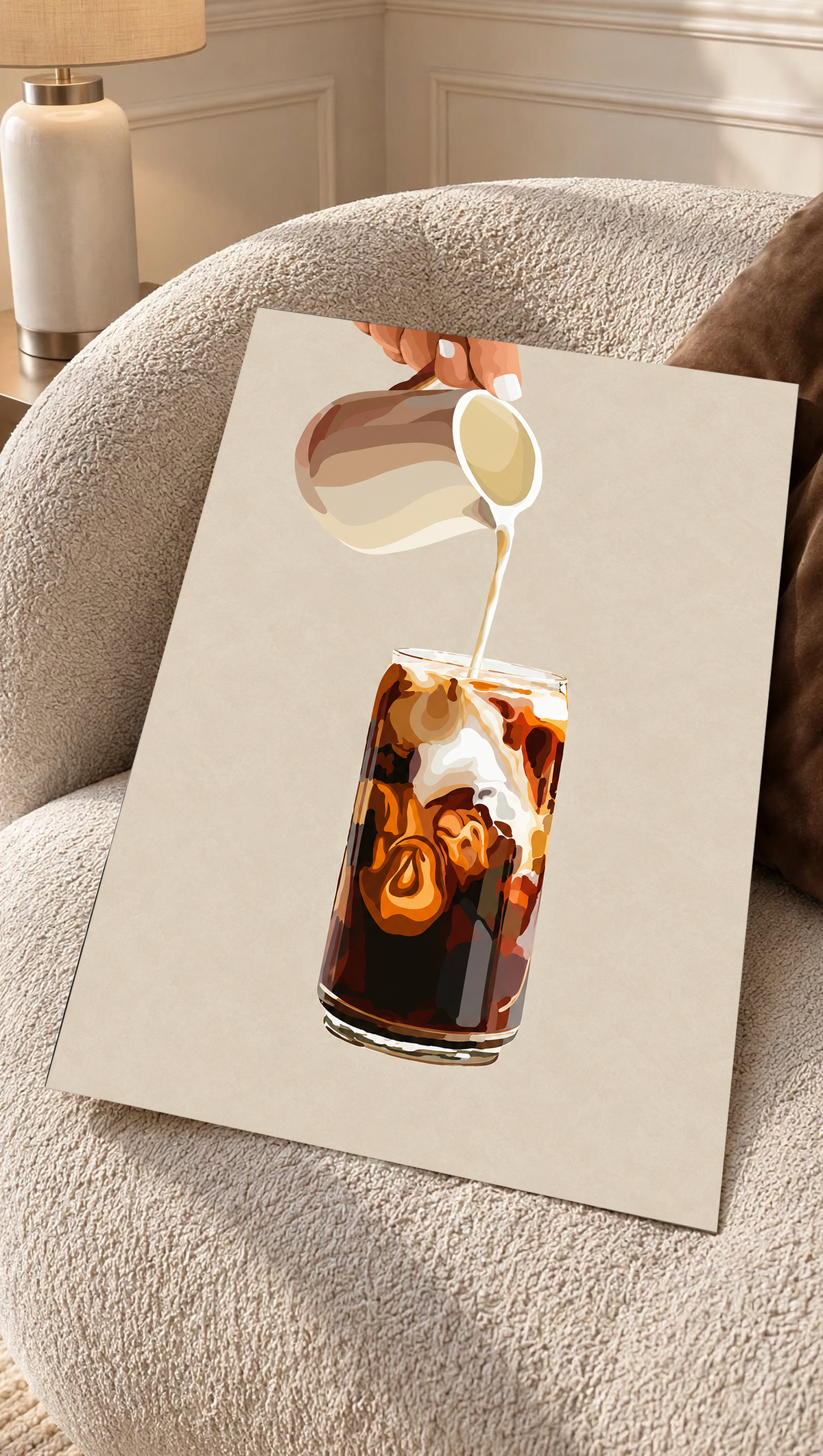 Mockup eines ungerahmten Drucks auf einem cremefarbenen Sessel mit strukturierter Oberfläche: Eiskaffeeillustration mit einer Hand, die Milch aus einem gestreiften Kännchen in ein hohes Glas gießt, und cremefarbenen Karamellwirbeln auf Beige.