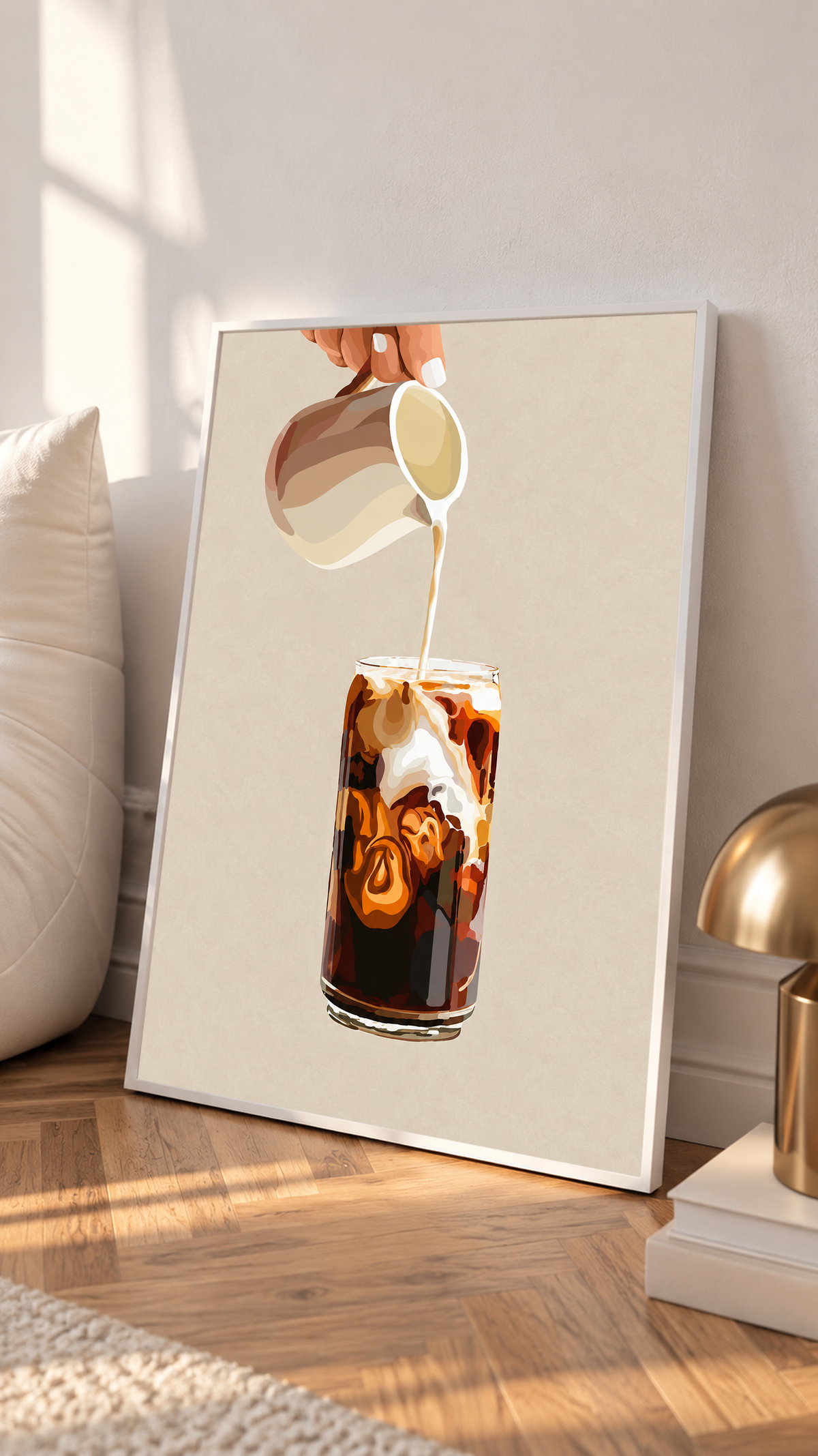 Mockup im weißen Rahmen, neben einem Kissen an eine helle Wand gelehnt: Eiskaffeeillustration mit einer Hand, die Milch aus einem gestreiften Kännchen in ein hohes Glas gießt, und cremefarbenen Karamellwirbeln auf Beige.