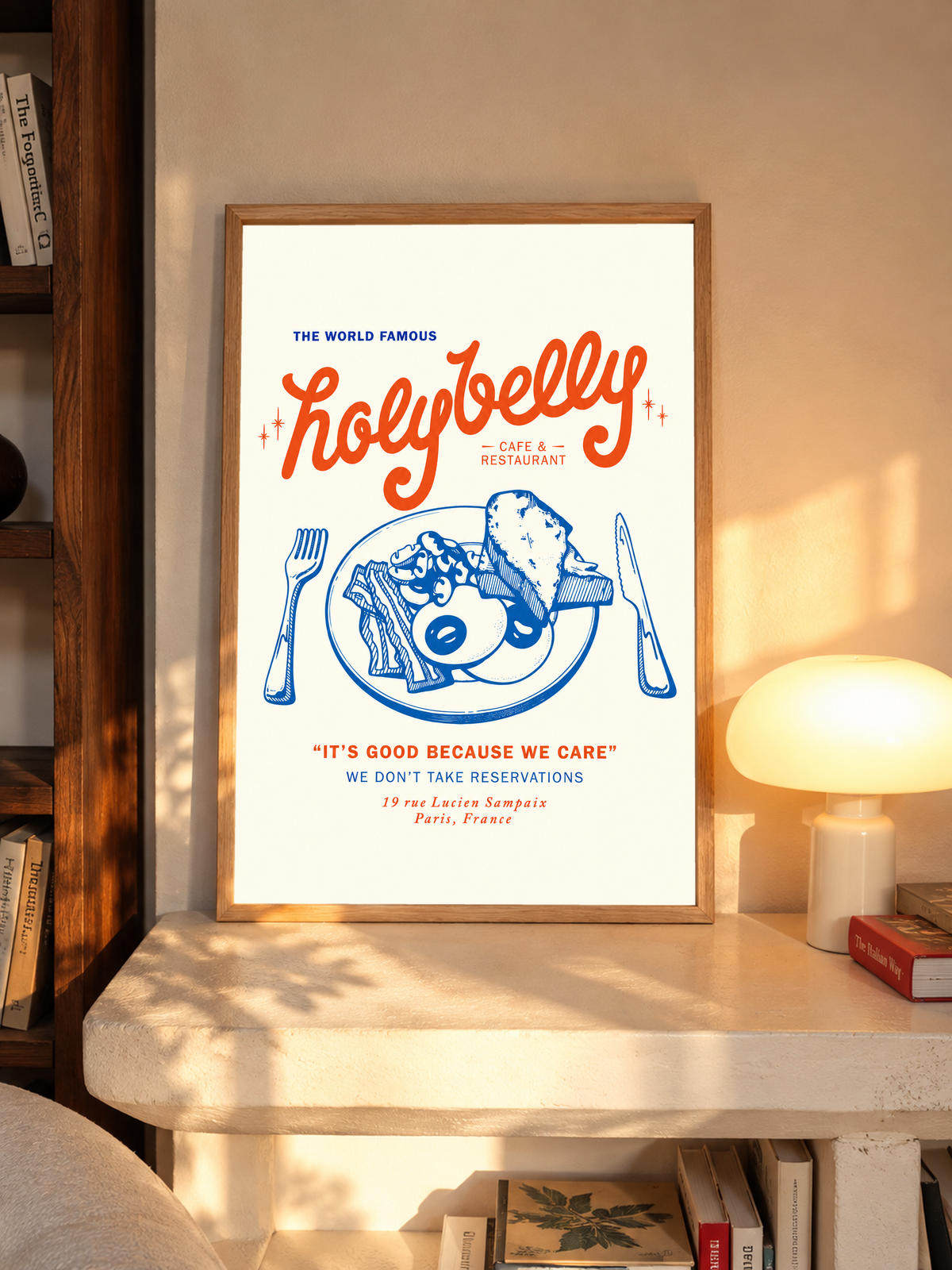 Ambientazione in cornice rovere su una mensola accanto a una lampada accesa: Illustrazione della colazione Holybelly con grandi scritte rosse, piatto blu con uova e pane tostato, forchetta, coltello e testi da caffetteria su crema.