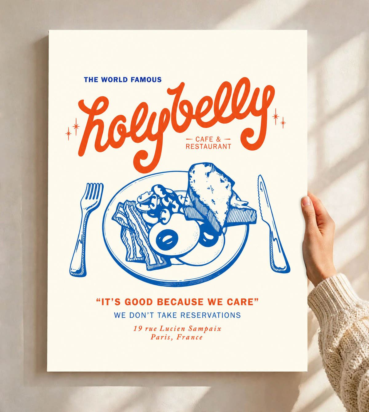 Ambientazione del poster senza cornice tenuto davanti a una parete chiara con luce dalla finestra: Illustrazione della colazione Holybelly con grandi scritte rosse, piatto blu con uova e pane tostato, forchetta, coltello e testi da caffetteria su crema.