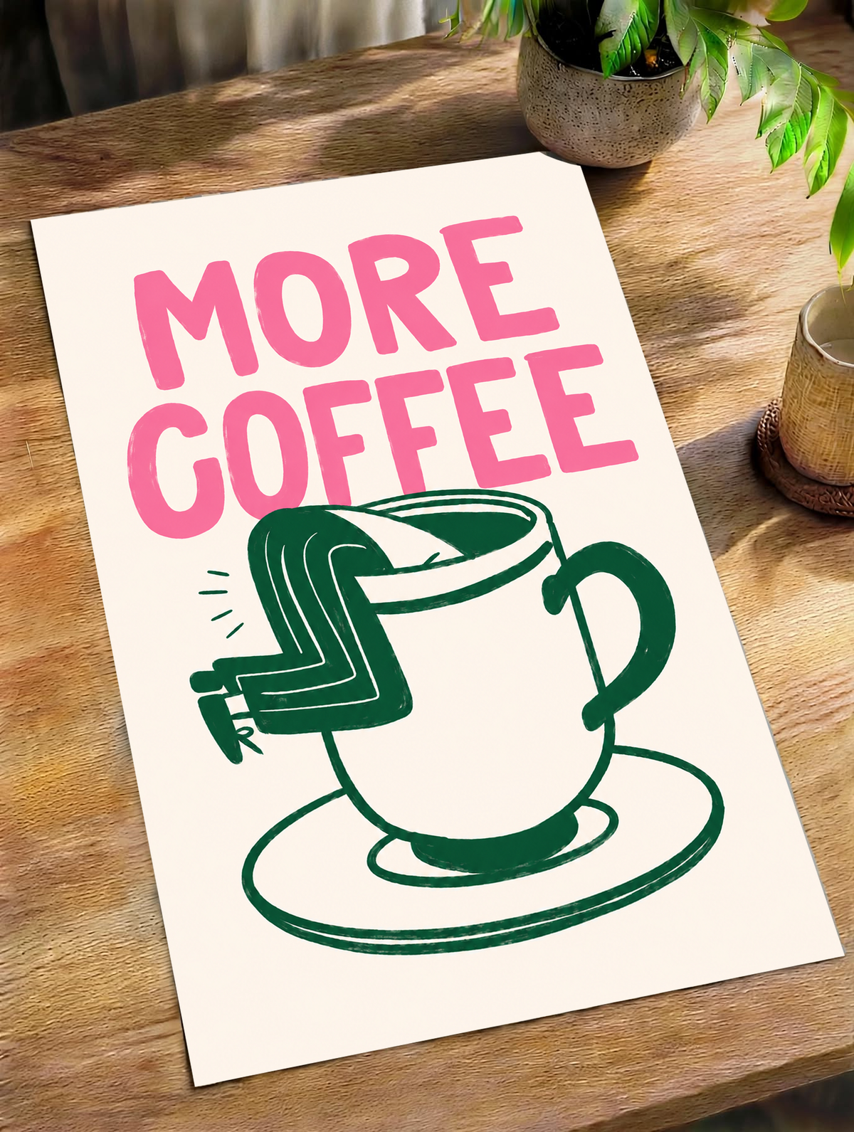 Mockup eines ungerahmten Posters auf einem Holztisch im Tageslicht: Großes rosa MORE COFFEE über einer grün gezeichneten Tasse mit Untertasse und einem Beinpaar über dem Rand auf Creme.