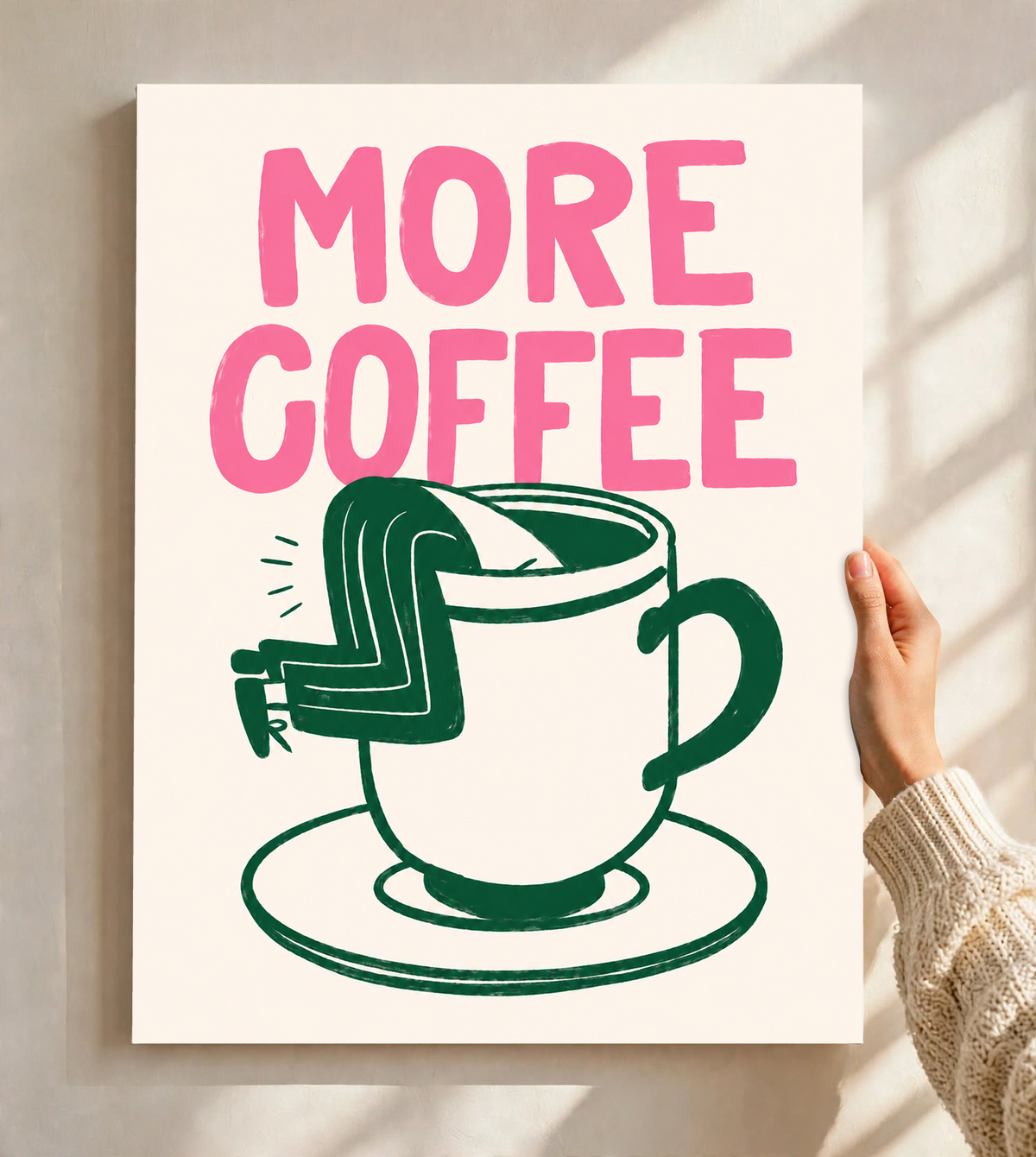 Mockup eines ungerahmten Posters, vor einer hellen Wand im Fensterlicht gehalten: Großes rosa MORE COFFEE über einer grün gezeichneten Tasse mit Untertasse und einem Beinpaar über dem Rand auf Creme.