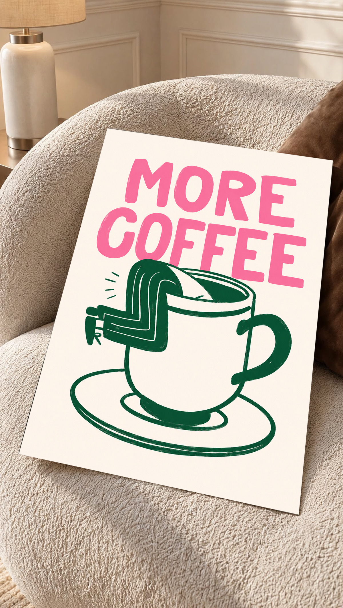 Mockup eines ungerahmten Drucks auf einem cremefarbenen Sessel mit strukturierter Oberfläche: Großes rosa MORE COFFEE über einer grün gezeichneten Tasse mit Untertasse und einem Beinpaar über dem Rand auf Creme.