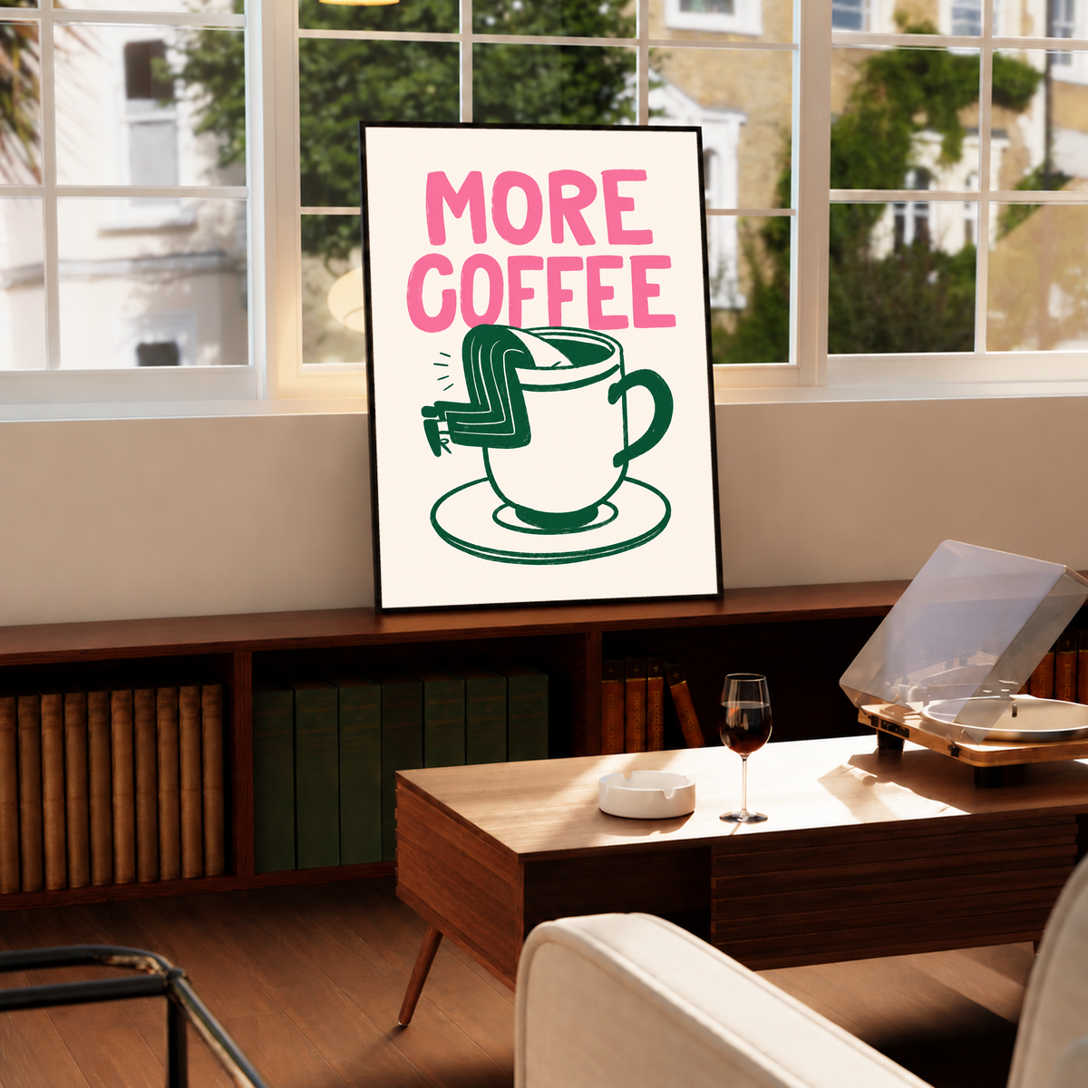 Raum-Mockup im schwarzen Rahmen über einem Plattenschrank unter einem breiten Fenster: Großes rosa MORE COFFEE über einer grün gezeichneten Tasse mit Untertasse und einem Beinpaar über dem Rand auf Creme.