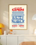 Ambientazione in cornice rovere sopra un mobile bianco con dettagli gialli: Yes, we are OPEN in rosso sopra un bar disegnato in blu con tenda, bancone, sgabelli, piante, orari e contatti di esempio su fondo crema.