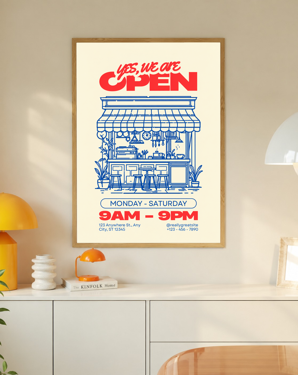 Mockup im Eichenrahmen über einem weißen Schrank mit gelben Akzenten: Rotes Yes, we are OPEN über einer blauen Cafézeichnung mit Markise, Theke, Hockern und Pflanzen sowie Beispielzeiten und Kontakttext auf Creme.