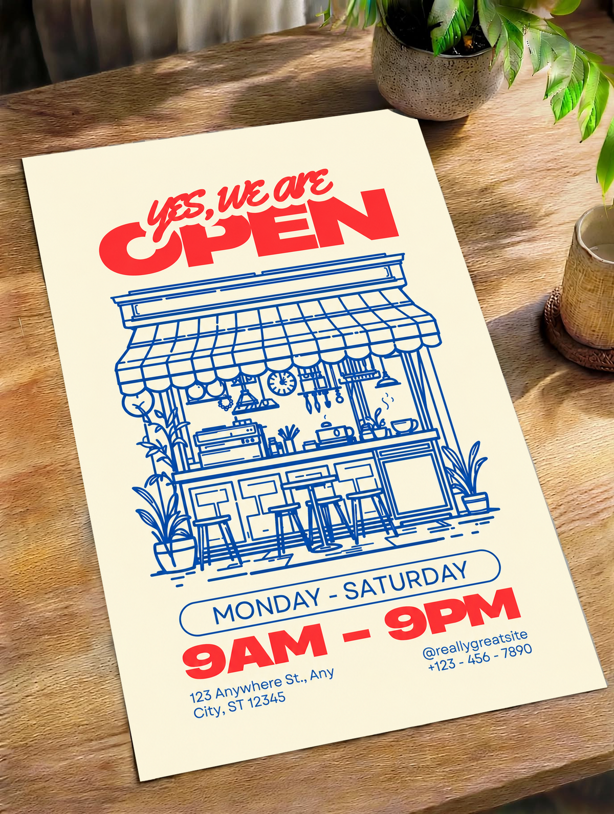 Ambientazione del poster senza cornice su un tavolo di legno alla luce naturale: Yes, we are OPEN in rosso sopra un bar disegnato in blu con tenda, bancone, sgabelli, piante, orari e contatti di esempio su fondo crema.