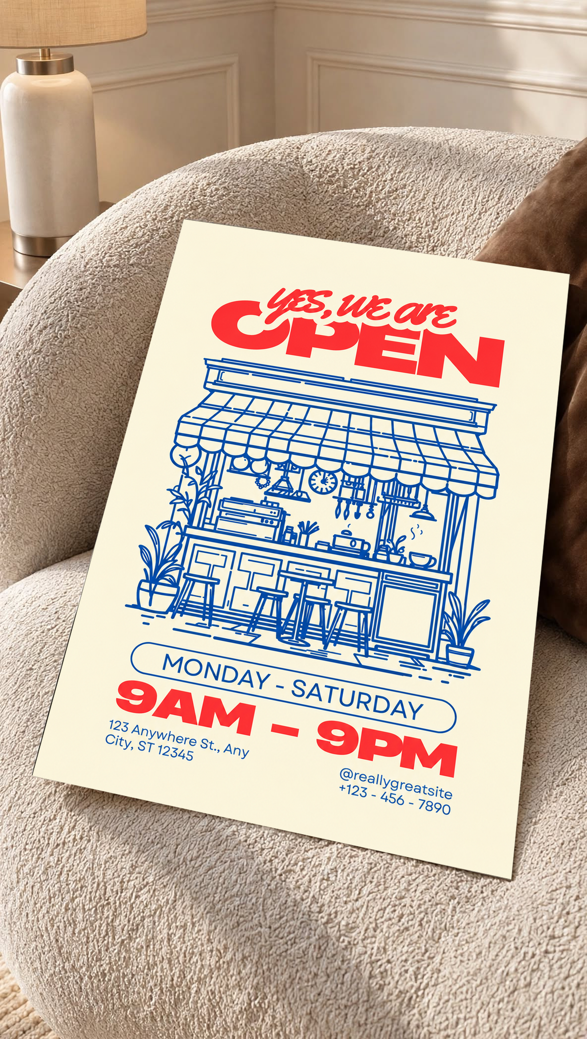 Ambientazione della stampa senza cornice su una poltrona crema dal tessuto strutturato: Yes, we are OPEN in rosso sopra un bar disegnato in blu con tenda, bancone, sgabelli, piante, orari e contatti di esempio su fondo crema.