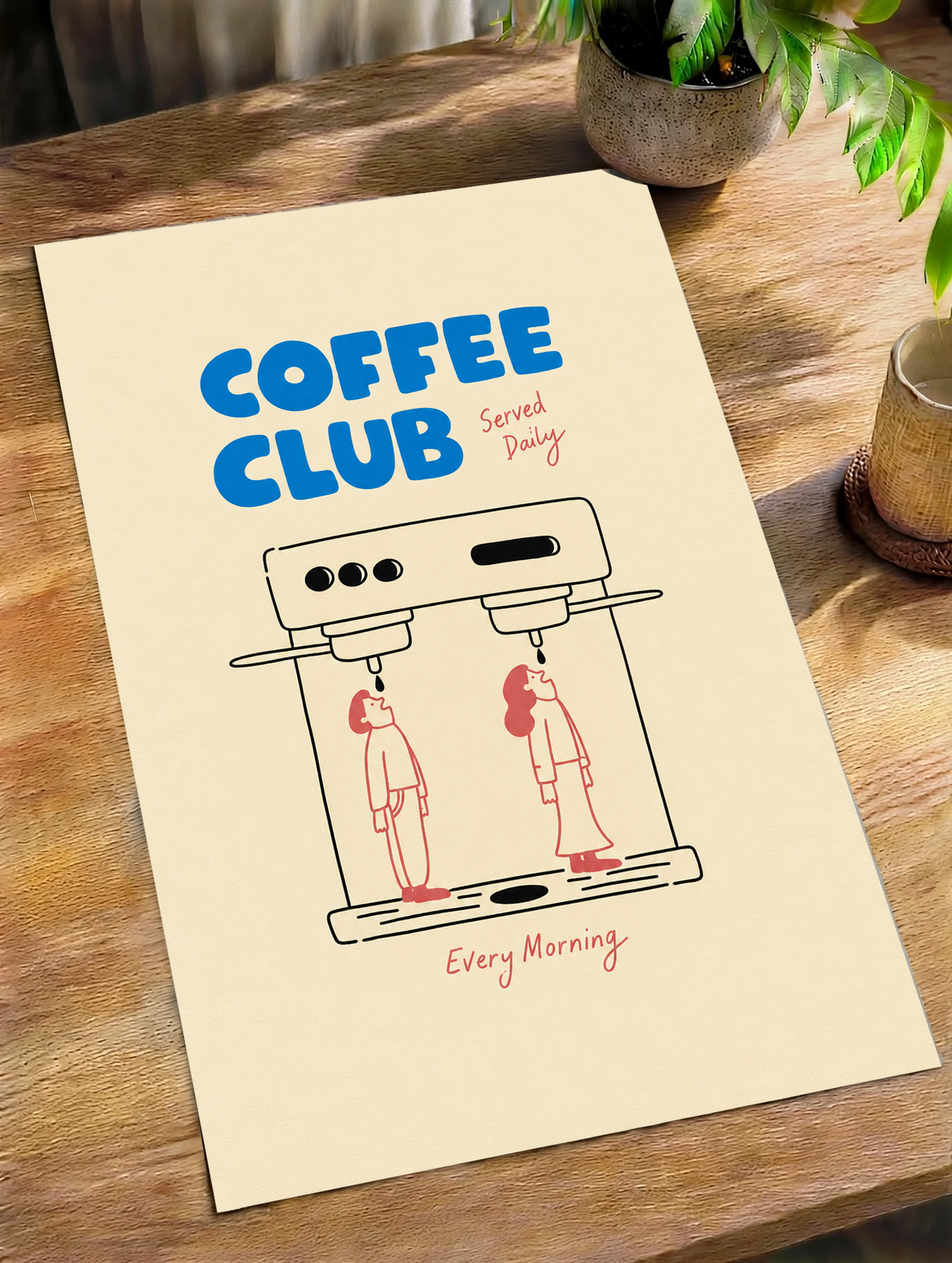 Blaues Coffee Club-Motiv mit schwarz gezeichneter Espressomaschine, zwei korallroten Figuren, roter Schrift und cremefarbenem Hintergrund. Ungerahmtes Poster schräg auf einem Holztisch neben Pflanze und Tasse.