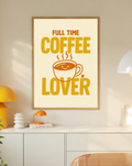 Full Time Coffee Lover-Motiv mit goldgelber Schrift, orangefarbener lächelnder Kaffeetasse, Dampf und kleinem Herz auf Creme. Im Eichenrahmen über einem weißen Schrank mit gelber Leuchte und kleiner orangefarbener Vase.