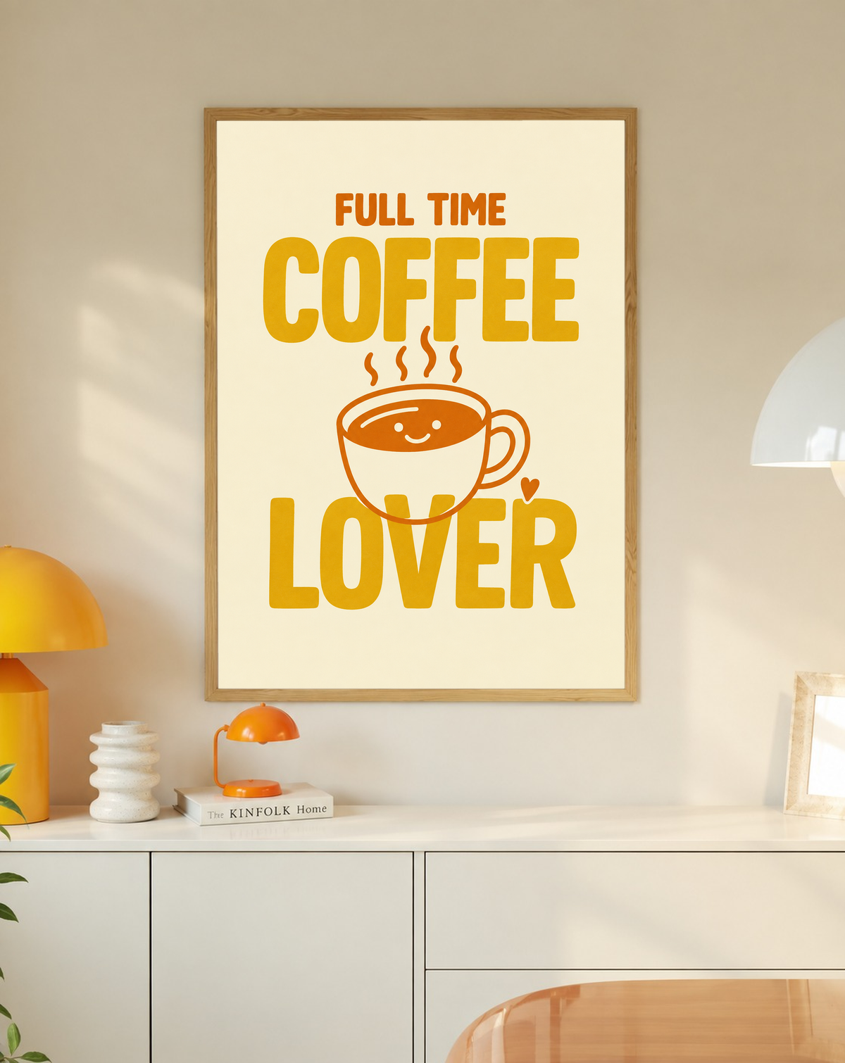 Full Time Coffee Lover-Motiv mit goldgelber Schrift, orangefarbener lächelnder Kaffeetasse, Dampf und kleinem Herz auf Creme. Im Eichenrahmen über einem weißen Schrank mit gelber Leuchte und kleiner orangefarbener Vase.