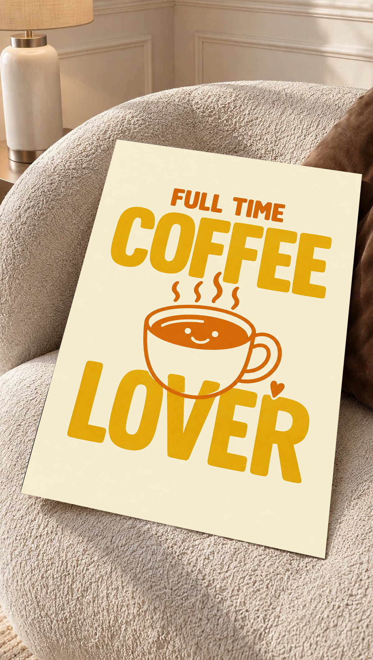 Full Time Coffee Lover-Motiv mit goldgelber Schrift, orangefarbener lächelnder Kaffeetasse, Dampf und kleinem Herz auf Creme. Ungerahmtes Poster auf einem strukturierten cremefarbenen Sessel.