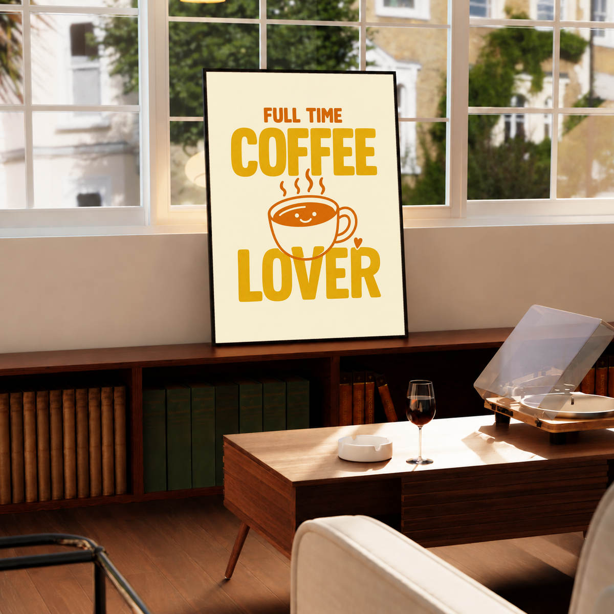 Full Time Coffee Lover-Motiv mit goldgelber Schrift, orangefarbener lächelnder Kaffeetasse, Dampf und kleinem Herz auf Creme. Im schwarzen Rahmen auf einem niedrigen Schrank unter einem Fenster, nahe Plattenspieler und Couchtisch.
