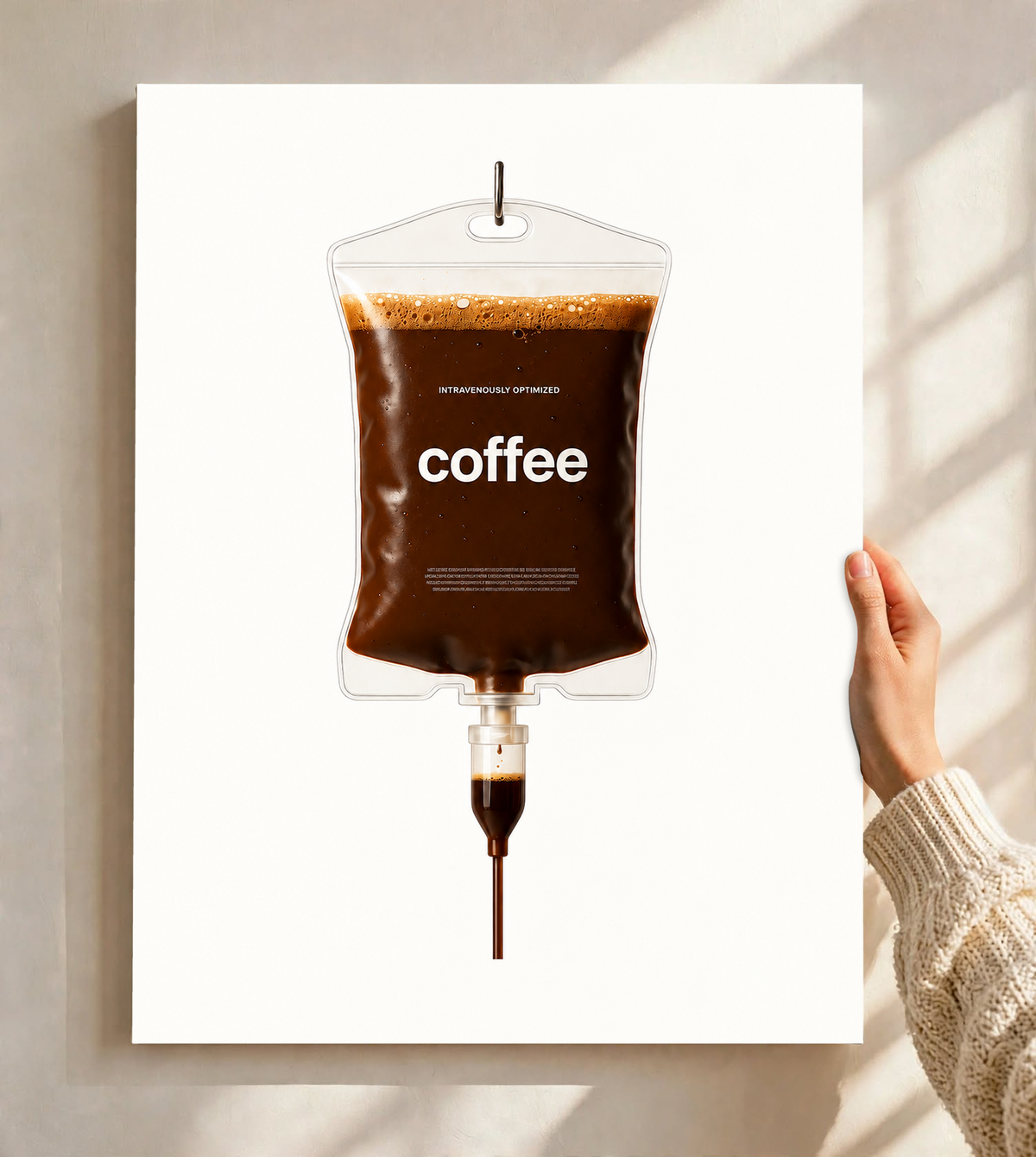 Ilustración surrealista Coffee IV con café marrón oscuro, burbujas de espuma dorada, bordes transparentes y etiqueta coffee sobre blanco. Póster sin marco sostenido ante una pared clara con sombras de ventana.