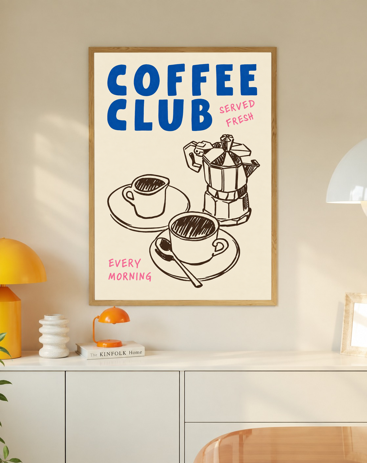 Blauer Schriftzug „Coffee Club“ mit rosa „Served Fresh“ und „Every Morning“ über einer braunen Mokkakanne und zwei Tassen auf Creme, in einem Eichenrahmen über einem weißen Schrank mit kleinen Lampen und Dekorationsobjekten.