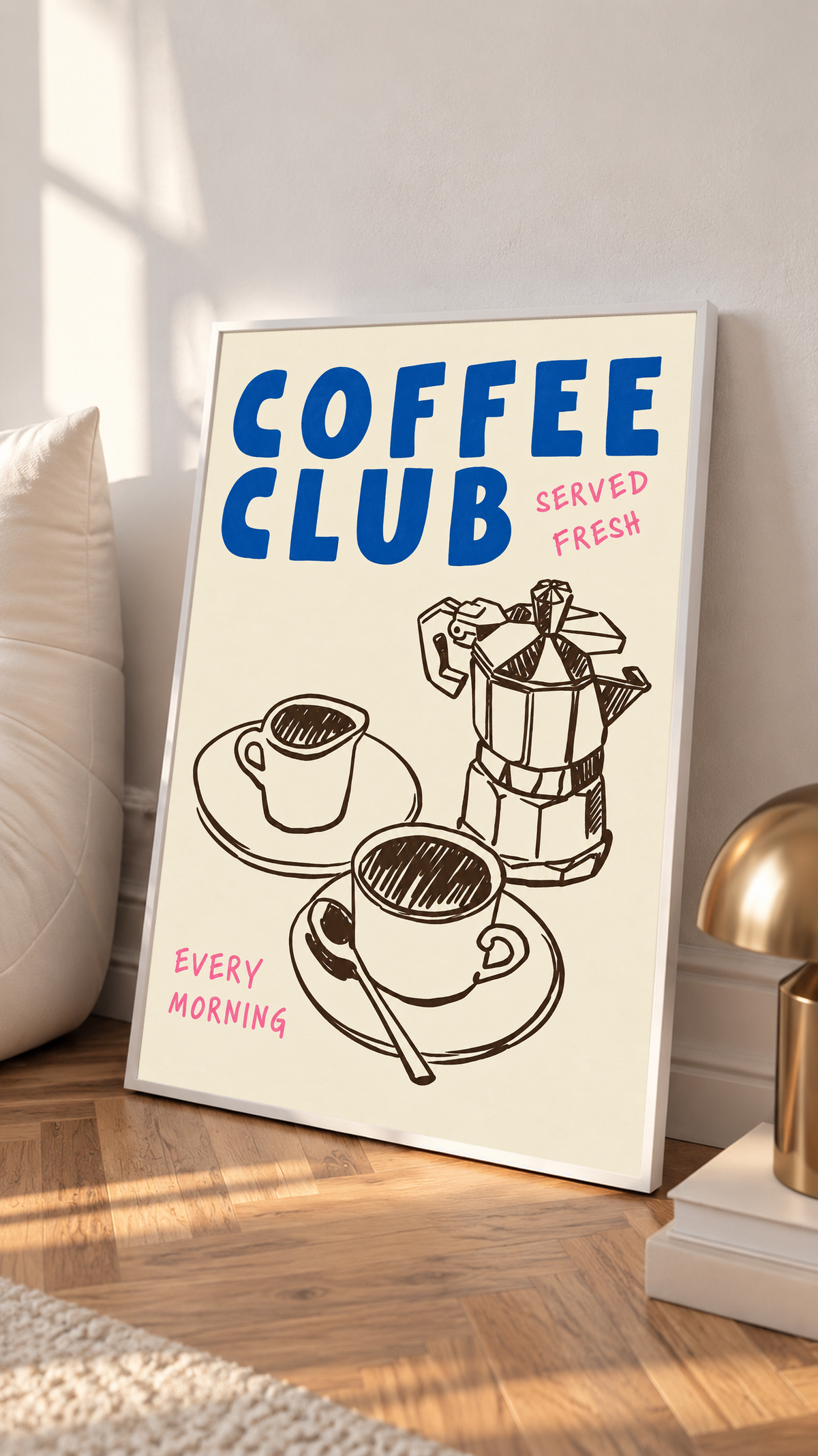 Blauer Schriftzug „Coffee Club“ mit rosa „Served Fresh“ und „Every Morning“ über einer braunen Mokkakanne und zwei Tassen auf Creme, in einem weißen Rahmen auf einem Holzboden, neben einem hellen Kissen und einer messingfarbenen Lampe.