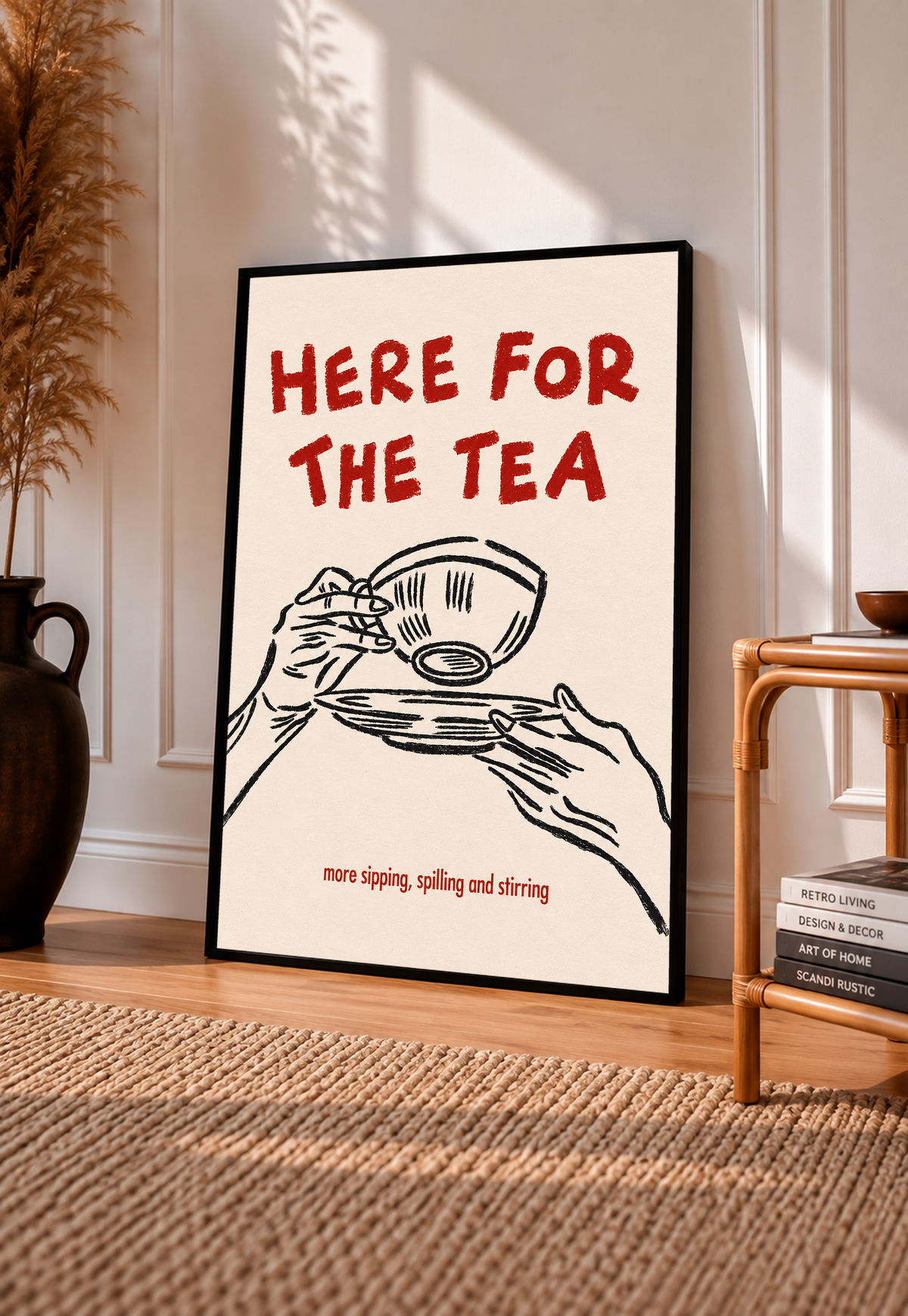 Roter Schriftzug „Here for the Tea“ über schwarz gezeichneten Händen mit Teetasse und Untertasse; darunter „more sipping, spilling and stirring“ auf Creme, in einem schwarzen Rahmen an einer sonnigen Wand mit Zierleisten, neben einem gewebten Teppich und einem kleinen Regal.