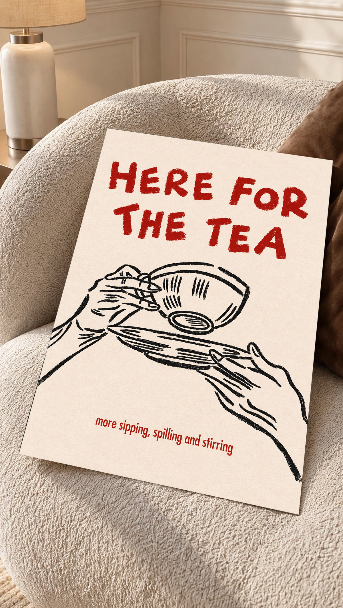 Roter Schriftzug „Here for the Tea“ über schwarz gezeichneten Händen mit Teetasse und Untertasse; darunter „more sipping, spilling and stirring“ auf Creme, als loses Poster auf einem cremefarbenen Sessel mit strukturierter Oberfläche.