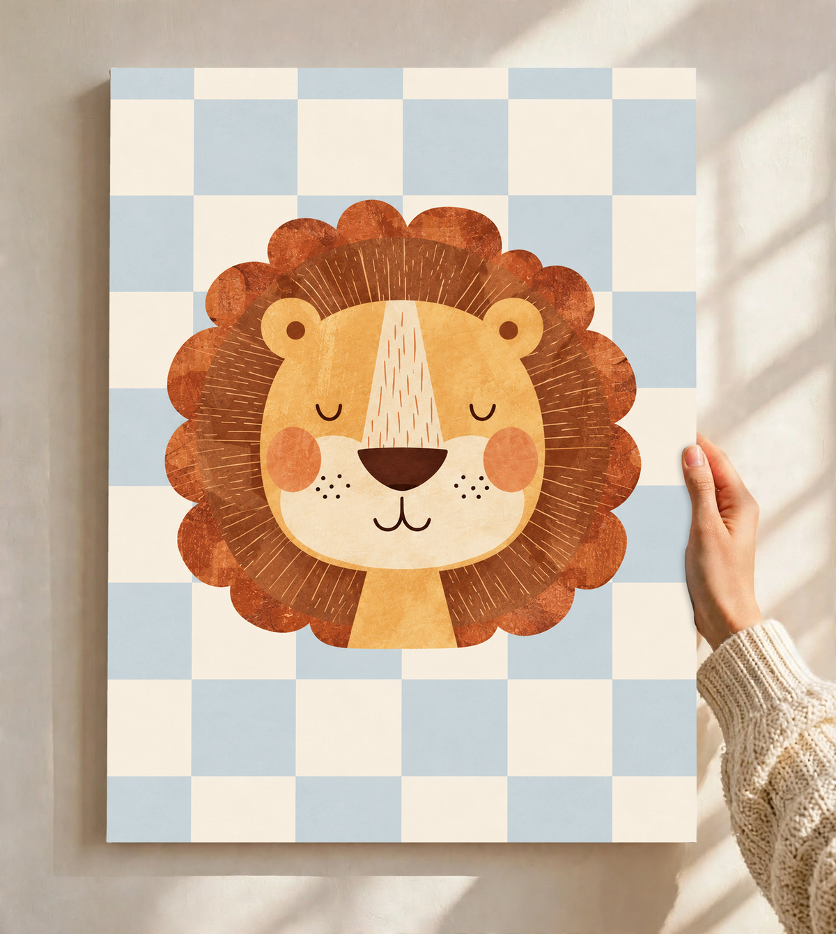 Rostro de león dorado con ojos cerrados, mejillas naranjas y melena ondulada marrón óxido sobre un damero azul claro y crema. Lámina sin marco sostenida ante una pared clara con luz solar y sombras de ventana.