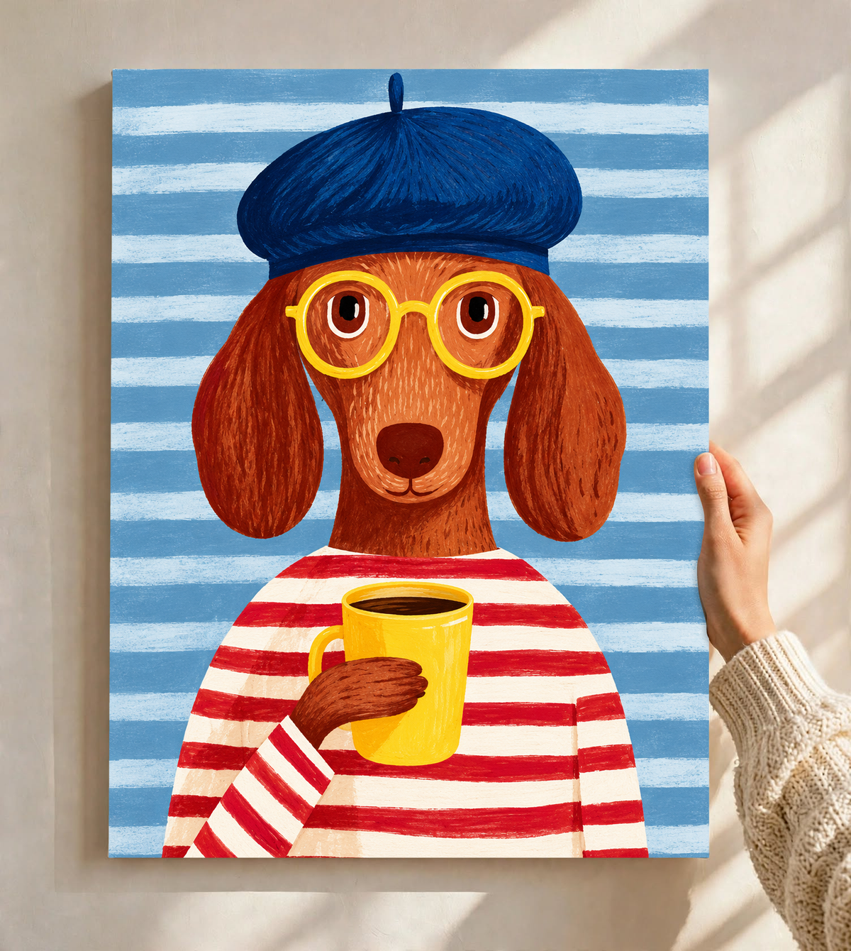 Lámina sin marco sostenida ante una pared clara con luz de ventana: Un perro marrón de orejas largas, boina azul, gafas amarillas y camiseta de rayas rojas y crema sostiene una taza amarilla ante un fondo de rayas azules.