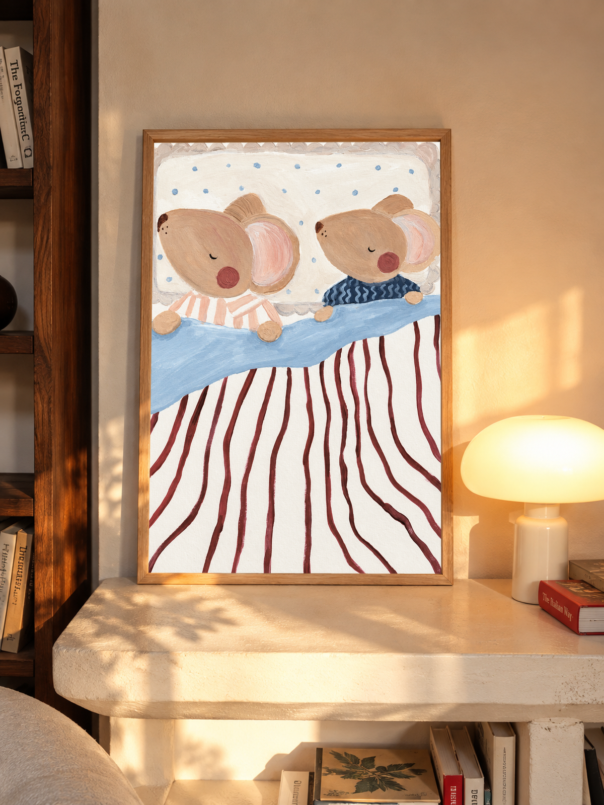 Dos ratones marrones dormidos y de mejillas rosadas, en pijamas de rayas melocotón y ondas azul marino, con ropa de cama azul, rayas burdeos y almohada punteada. En un marco de tono roble sobre una repisa junto a una lámpara encendida.