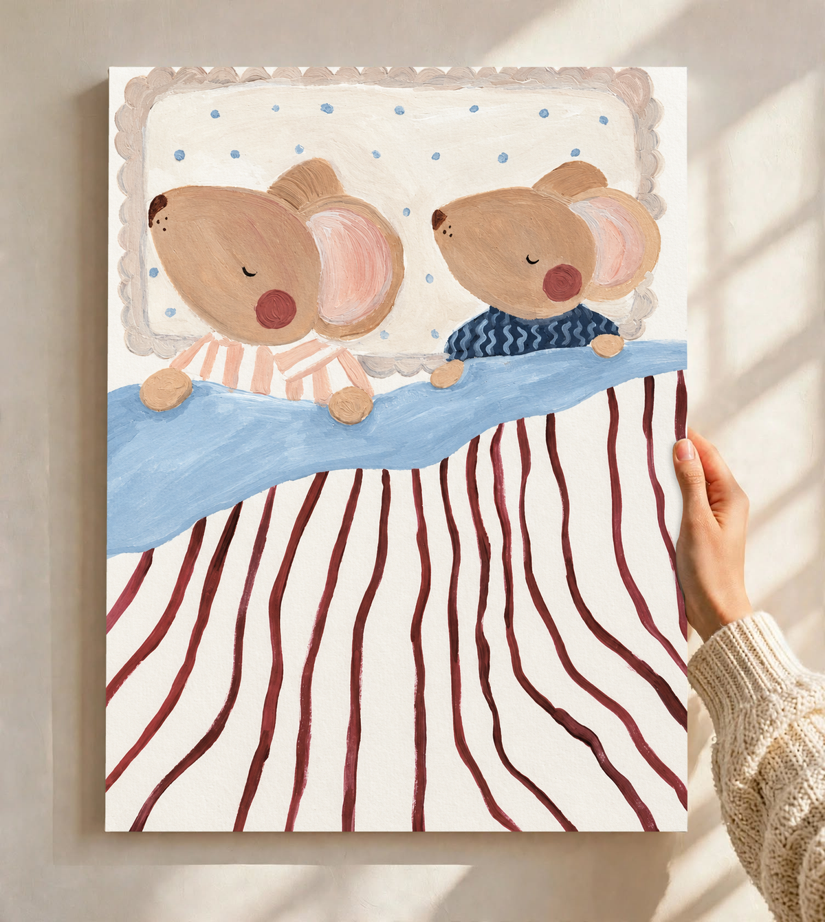 Dos ratones marrones dormidos y de mejillas rosadas, en pijamas de rayas melocotón y ondas azul marino, con ropa de cama azul, rayas burdeos y almohada punteada. Lámina sin marco sostenida ante una pared clara con luz solar y sombras de ventana.