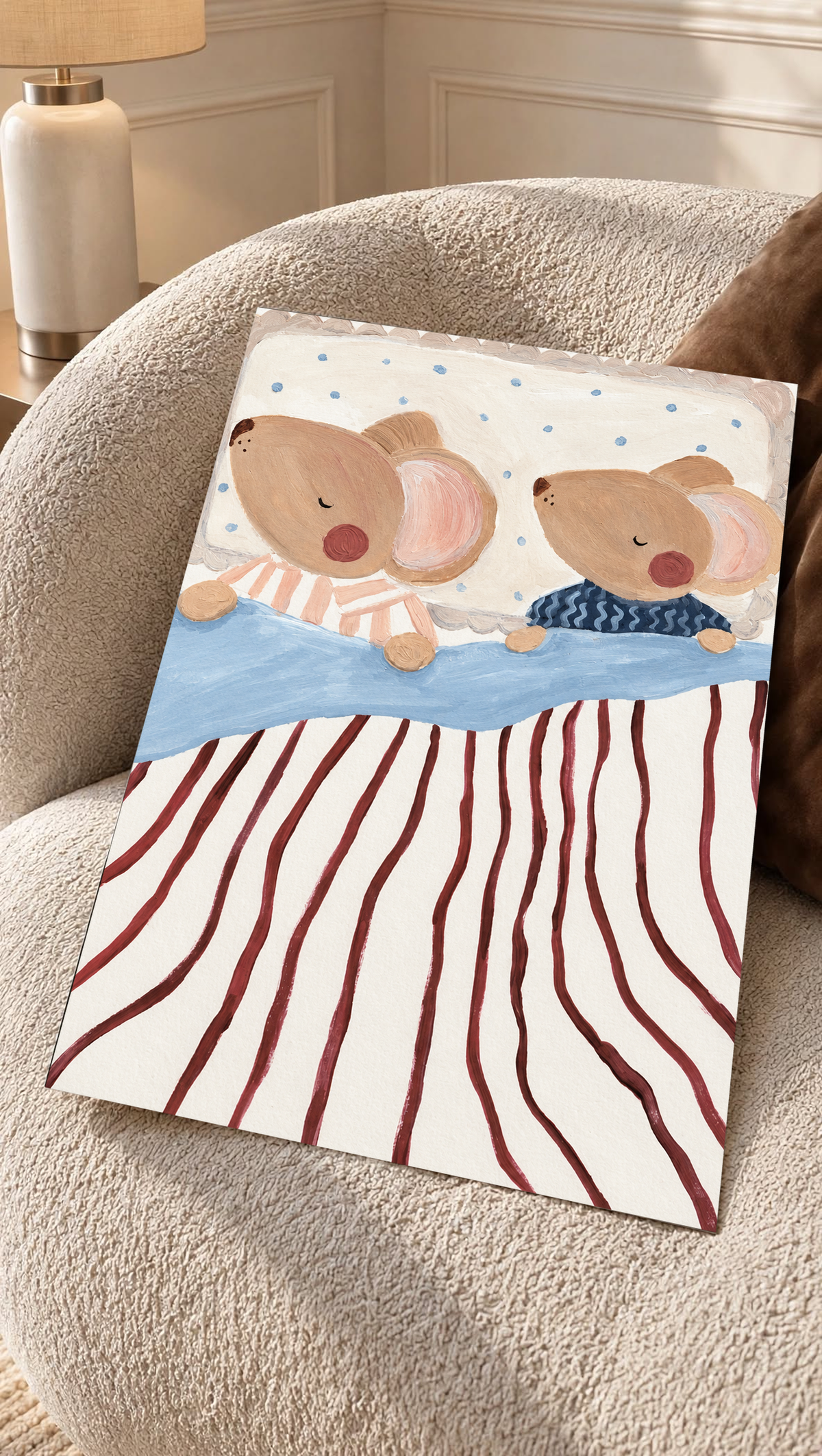 Dos ratones marrones dormidos y de mejillas rosadas, en pijamas de rayas melocotón y ondas azul marino, con ropa de cama azul, rayas burdeos y almohada punteada. Lámina sin marco apoyada sobre un sillón de textura color crema.
