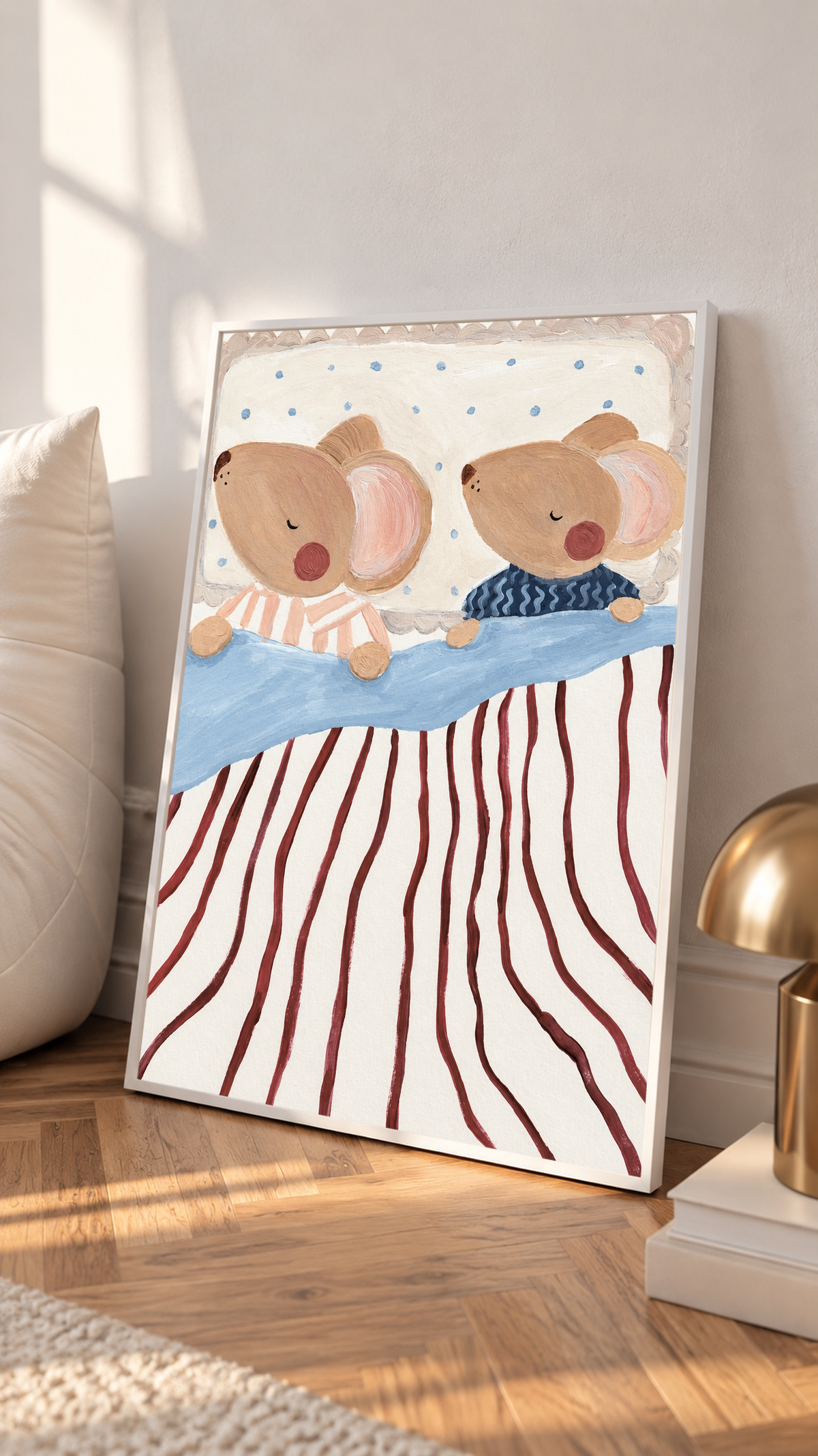 Dos ratones marrones dormidos y de mejillas rosadas, en pijamas de rayas melocotón y ondas azul marino, con ropa de cama azul, rayas burdeos y almohada punteada. Marco blanco apoyado junto a cojines contra una pared clara, cerca de una lámpara de tono latón.