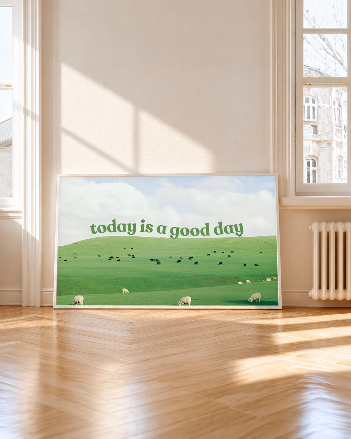 Grüne Schrift 'today is a good day' über Weiden mit Schafen, kleinen Rindern und hellem Wolkenhimmel. Weißer Rahmen neben einem hohen Fenster mit Sonnenlicht und Schatten auf dem Holzboden.