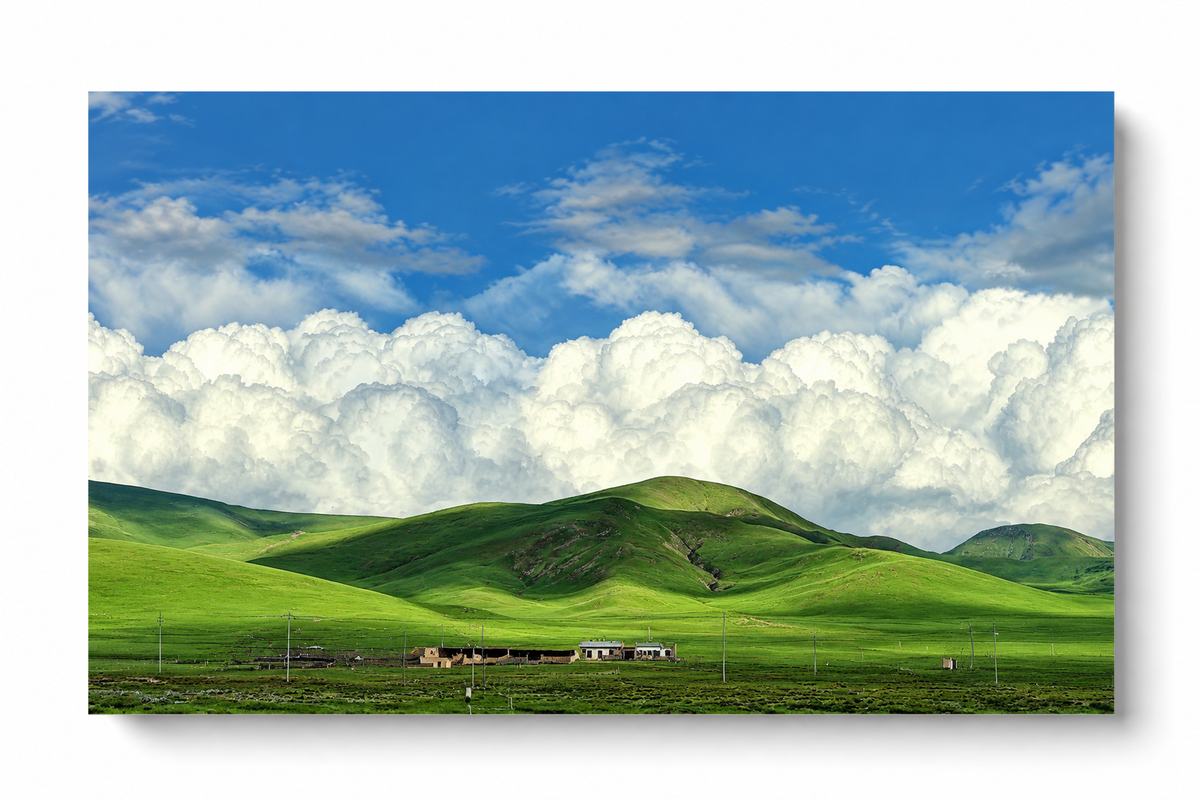 Colline verdi arrotondate e piccoli edifici rurali sotto grandi nuvole bianche e un cielo azzurro luminoso. Poster orizzontale senza cornice su fondo bianco con una morbida ombra.