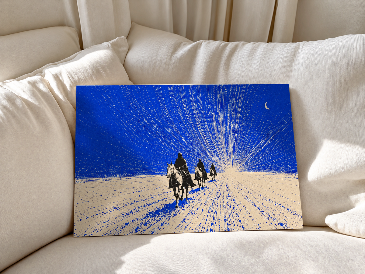 Tres jinetes oscuros se acercan sobre terreno crema bajo un cielo cobalto, una luna creciente y trazos finos radiantes. Póster sin marco apoyado en cojines blancos de sofá.