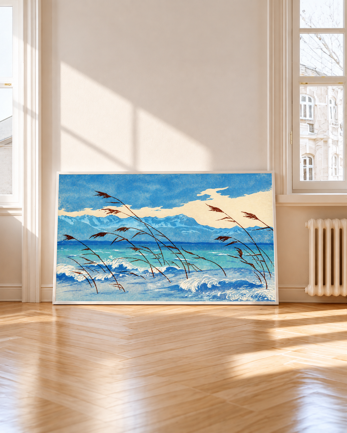 Russet reeds bend over curling blue and cream waves, with turquoise water, a distant mountain ridge and broad pale clouds behind. White frame by a tall window, with sunlight and shadows across a wooden floor.