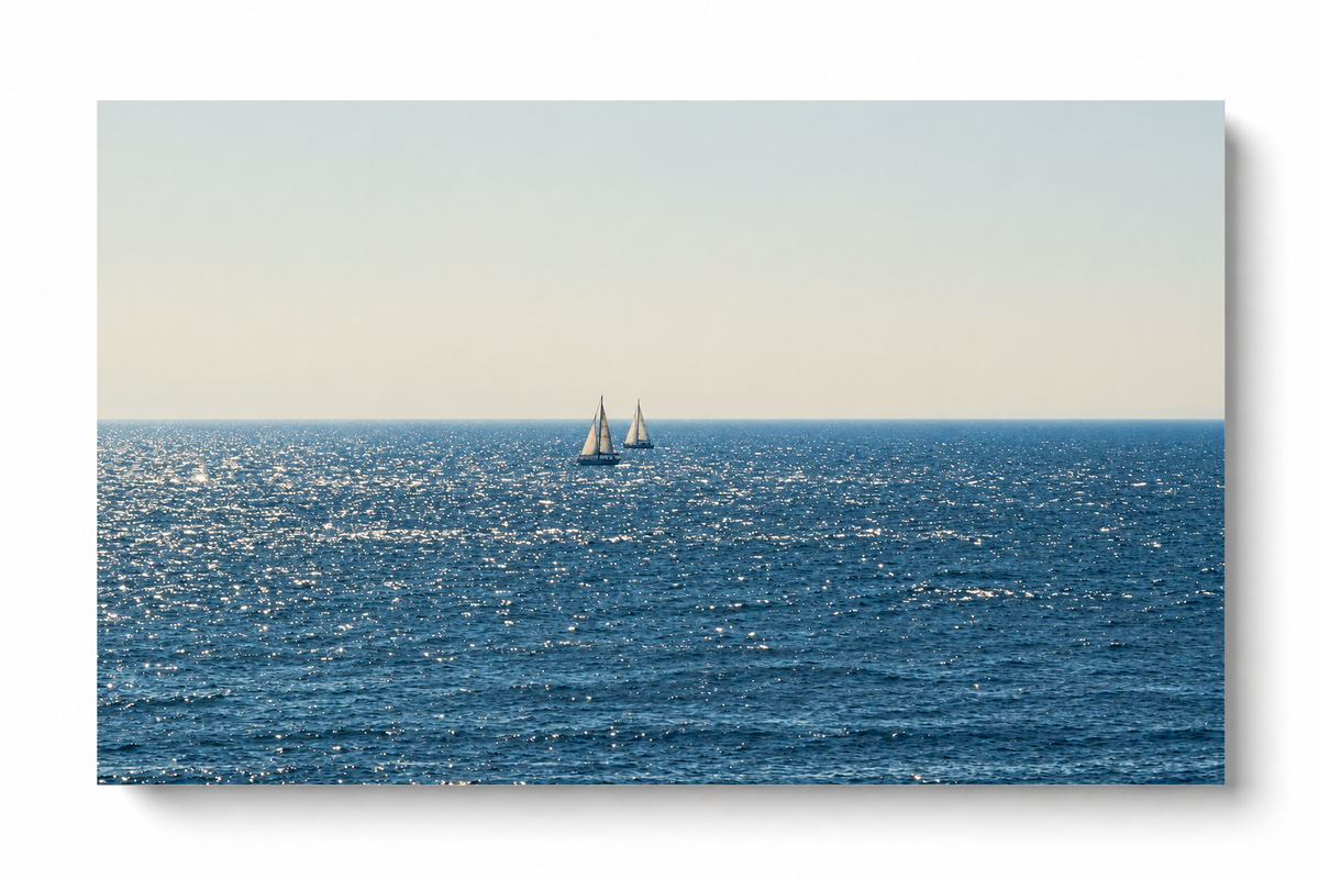 Due barche lontane dalle vele bianche vicino all’orizzonte sul mare blu scintillante sotto un ampio cielo chiaro crema-grigio. Poster orizzontale senza cornice su fondo bianco con una morbida ombra.