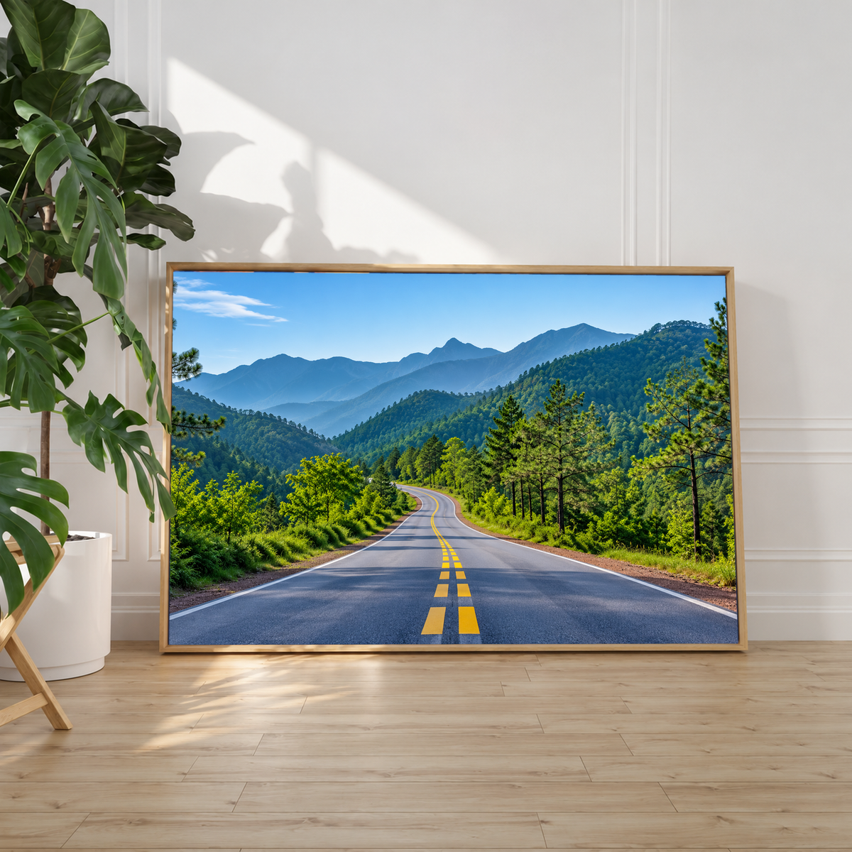 Eine gewundene Straße mit gelber Mittellinie führt durch grünen Wald zu gestaffelten Bergketten unter blassblauem Himmel. Heller Schattenfugenrahmen an einer weißen Wand neben einer Zimmerpflanze; Sonnenlicht auf dem Holzboden.