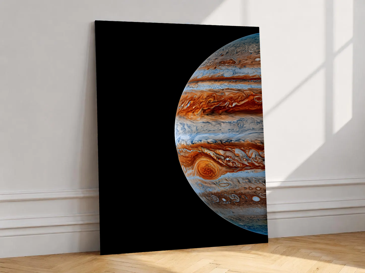 Close-up Jupiter artwork with orange-brown and blue-white cloud bands and the Great Red Spot on black, shown unframed on a white wall above parquet flooring with a diagonal sun shadow