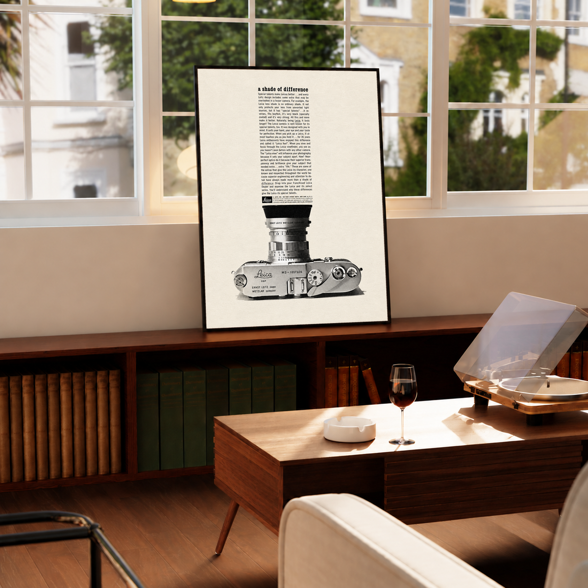A monochrome Leica camera beneath a tall column of advertising typography in a black frame by a bright window above a record player