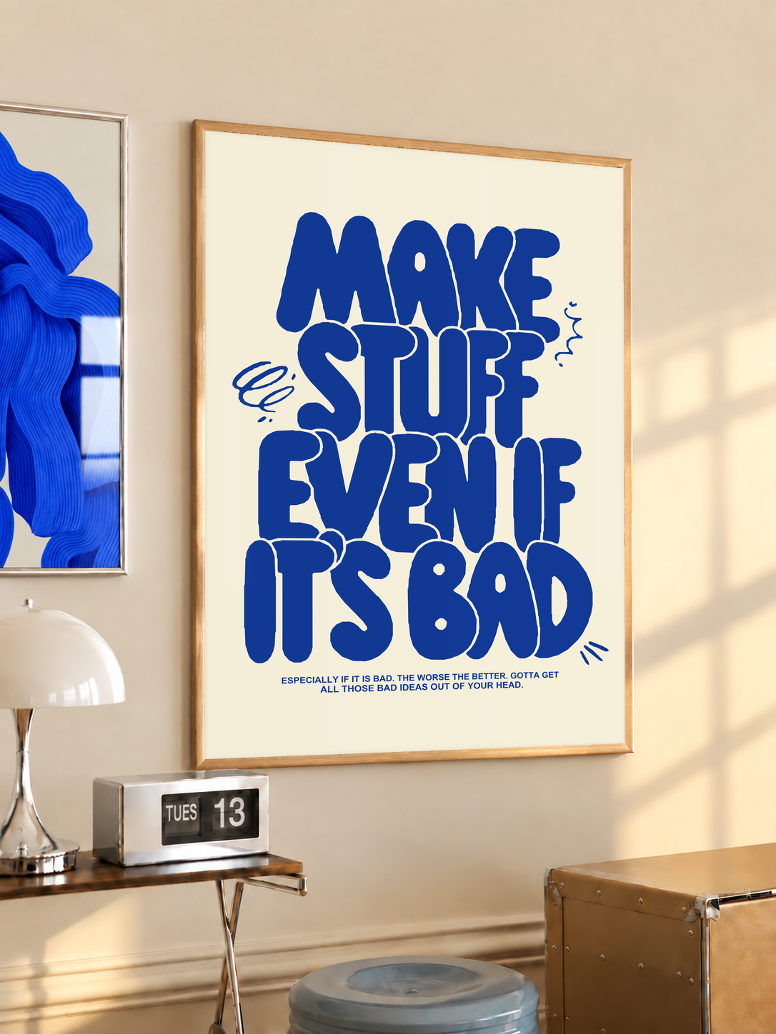 Framed cream poster with bold blue text reading “MAKE STUFF EVEN IF IT'S BAD”.