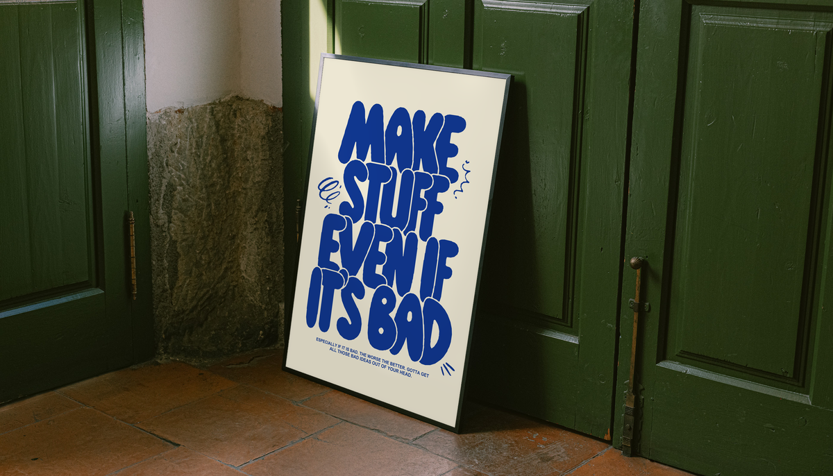 Framed cream poster with bold blue “MAKE STUFF EVEN IF IT'S BAD” lettering on the floor.