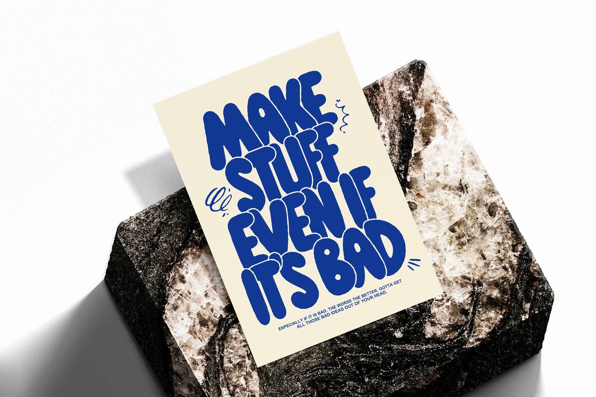 Cream poster with bold blue “MAKE STUFF EVEN IF IT'S BAD” laid on a stone surface.