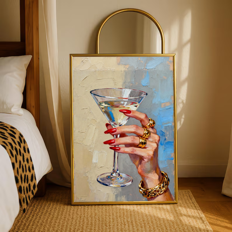 Gold-framed hand print artwork: martini glass, red nails and gold rings on blue