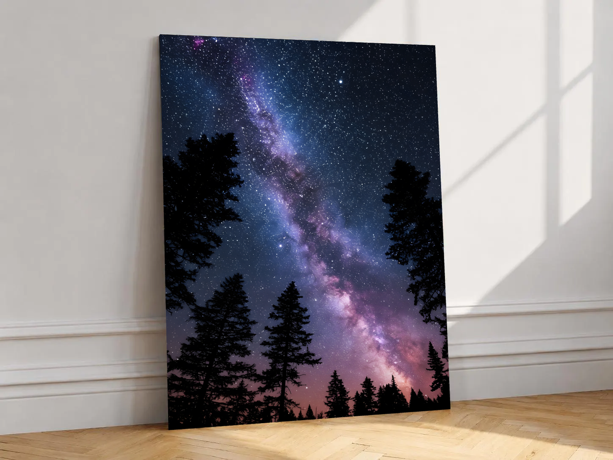 Violet-pink Milky Way band across a dark blue starry sky above black conifer silhouettes, shown unframed on a white wall above parquet flooring with a diagonal sun shadow