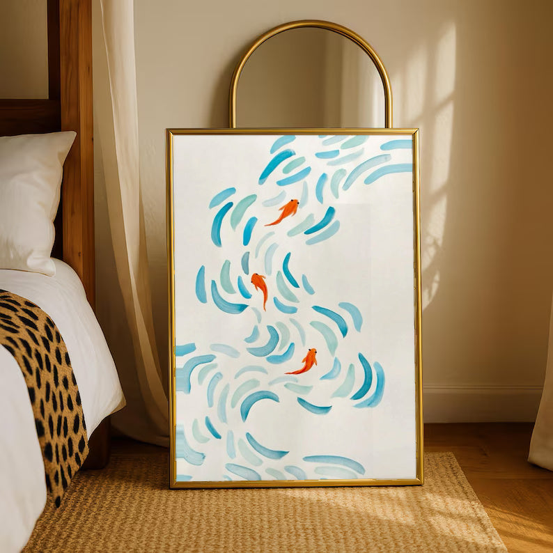 Small orange koi swimming among curved aqua and blue brushstrokes on cream in a gold-tone styling frame leaning beside a bedroom mirror