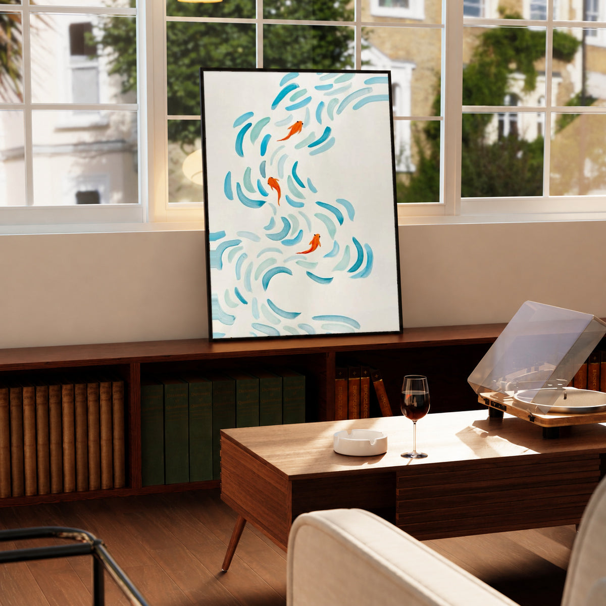 Small orange koi swimming among curved aqua and blue brushstrokes on cream in a black display frame on a wooden console beside a sunlit window